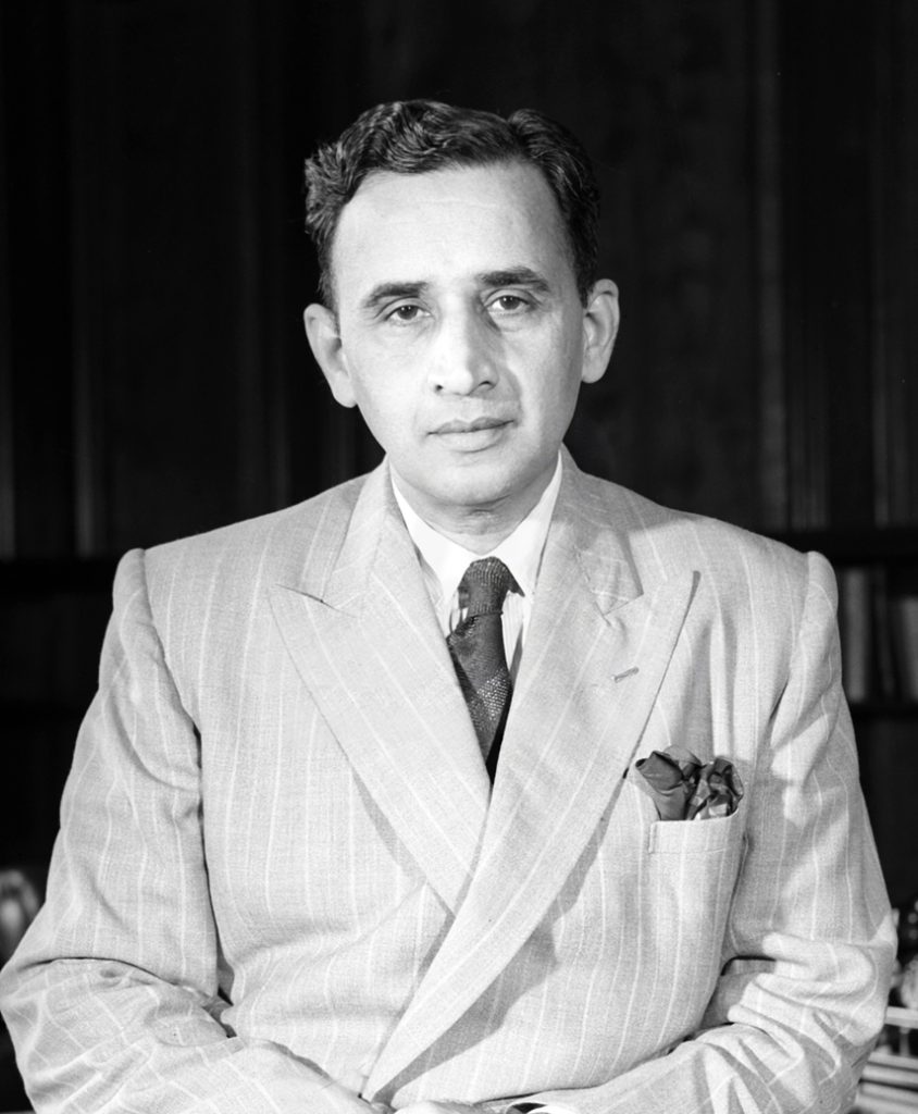 A black-and-white photograph of C. D. Deshmukh seated, in a light suit
