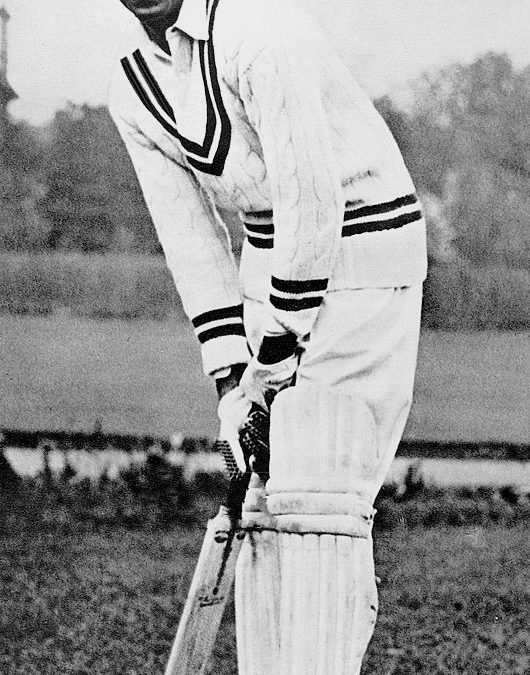 A black-and-white photograph of C. K. Nayudu in cricket whites, holding a bat