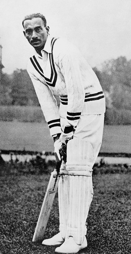 A black-and-white photograph of C. K. Nayudu in cricket whites, holding a bat