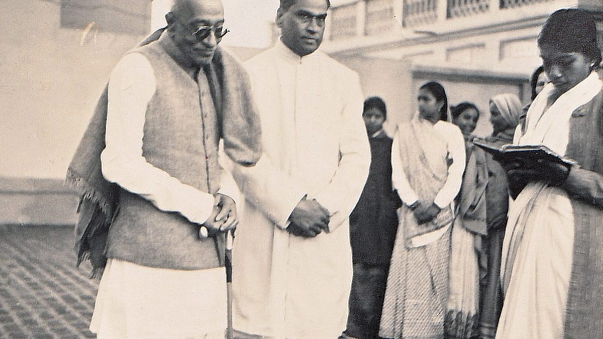 A black-and-white photograph of C. Rajagopalachari in dark glasses standing beside V. A. Sundaram