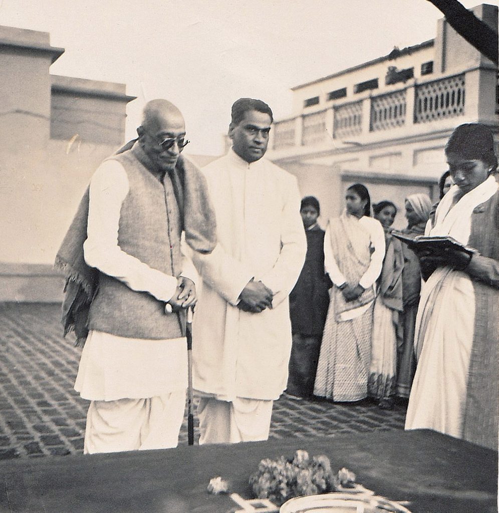 A black-and-white photograph of C. Rajagopalachari in dark glasses standing beside V. A. Sundaram