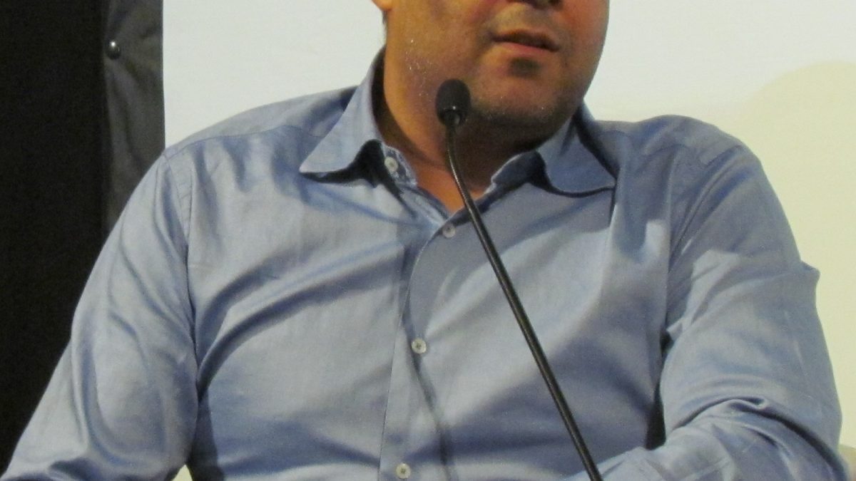 Chetan Bhagat in a dark shirt speaking at a book event
