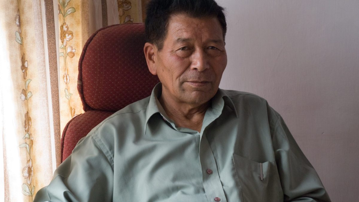 Chewang Norphel in a green shirt seated in an armchair by a window