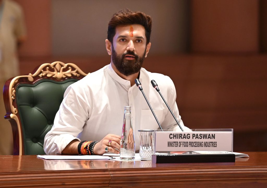 Chirag Paswan in a white kurta seated at a desk with microphones and his name plate