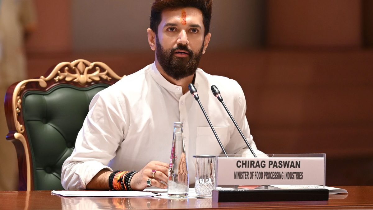 Chirag Paswan in a white kurta seated at a desk with microphones and his name plate