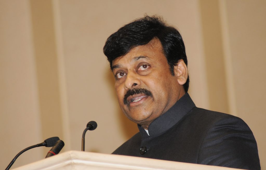 Chiranjeevi with a moustache, in a dark bandhgala, speaking at a lectern