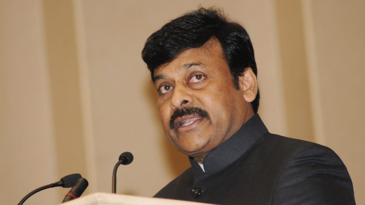Chiranjeevi with a moustache, in a dark bandhgala, speaking at a lectern