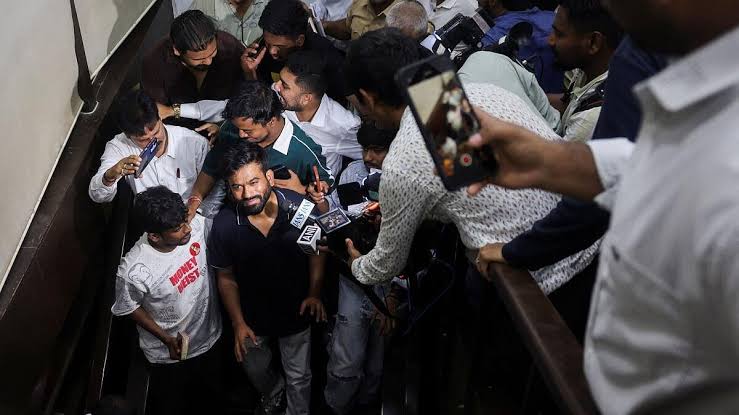 Journalists crowd around a man in a black shirt as he is detained and questioned