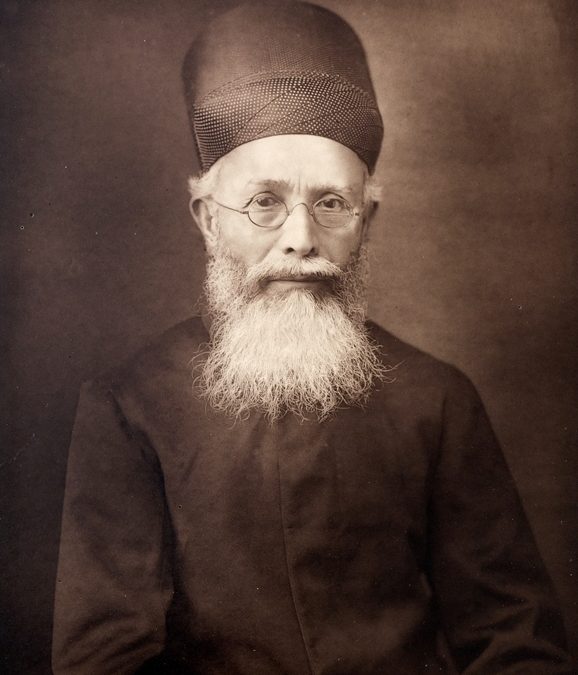 A photograph of Dadabhai Naoroji with a white beard, in a cap and dark coat