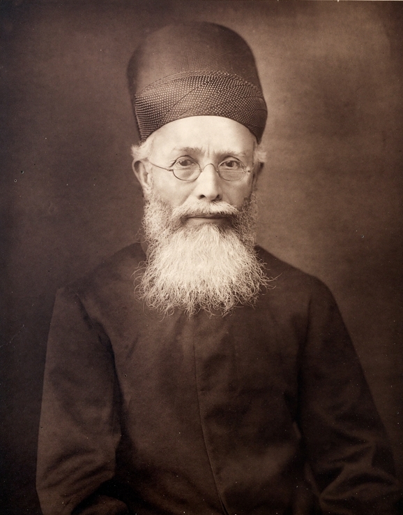 A photograph of Dadabhai Naoroji with a white beard, in a cap and dark coat