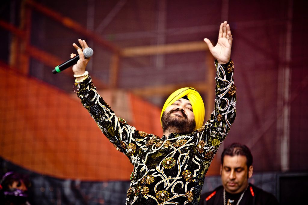 Daler Mehndi in a yellow turban singing on stage with one arm raised