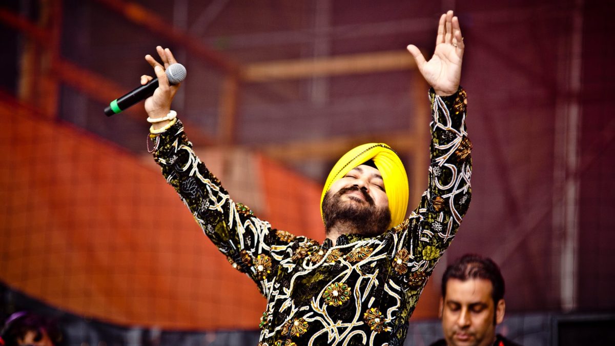 Daler Mehndi in a yellow turban singing on stage with one arm raised
