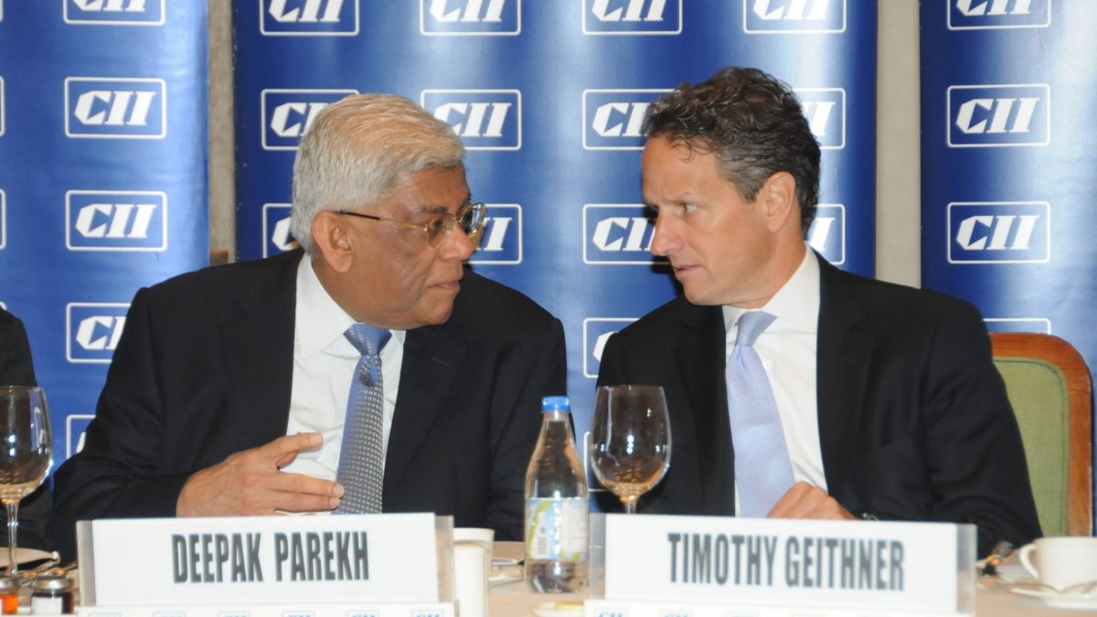 Deepak Parekh seated at a meeting table beside Timothy Geithner