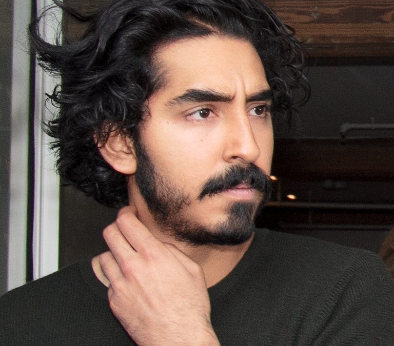 Dev Patel with a beard, in a dark jacket
