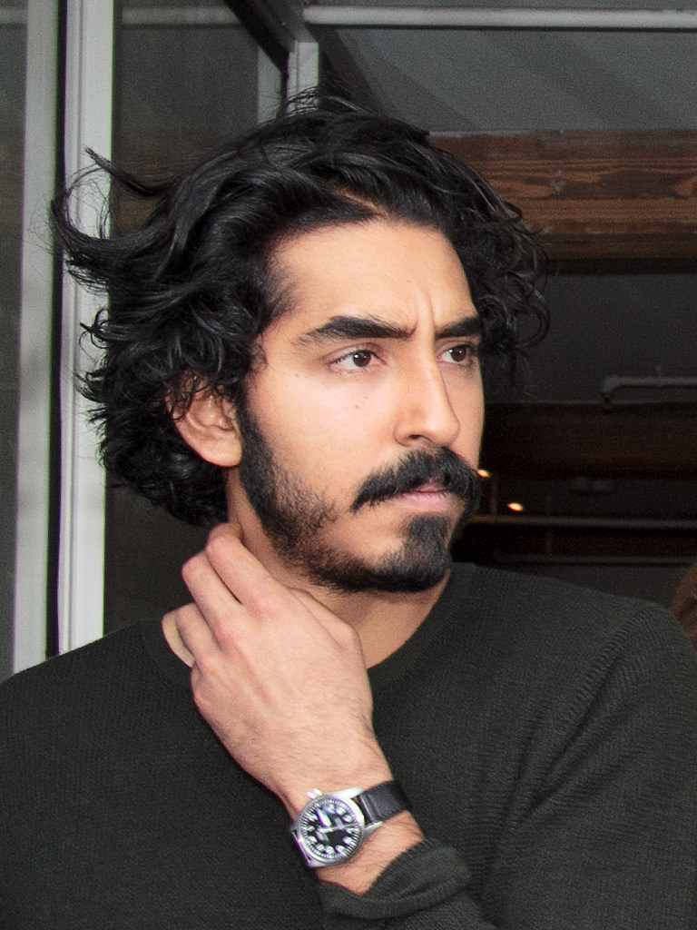 Dev Patel with a beard, in a dark jacket