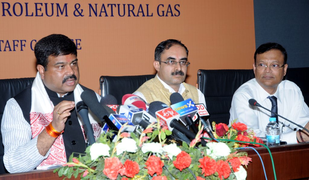 Dharmendra Pradhan in glasses and a waistcoat speaking into a bank of press microphones