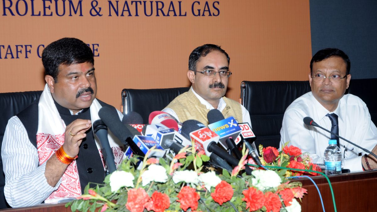 Dharmendra Pradhan in glasses and a waistcoat speaking into a bank of press microphones