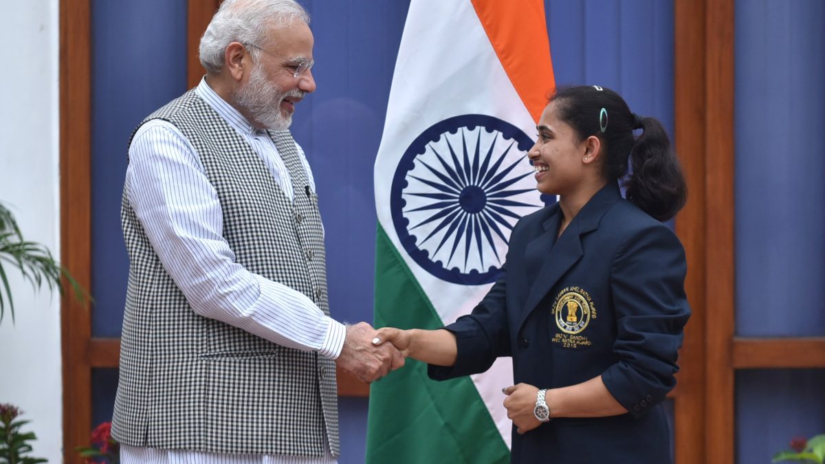 Dipa Karmakar in a navy blazer shaking hands with Prime Minister Narendra Modi beside the Indian flag