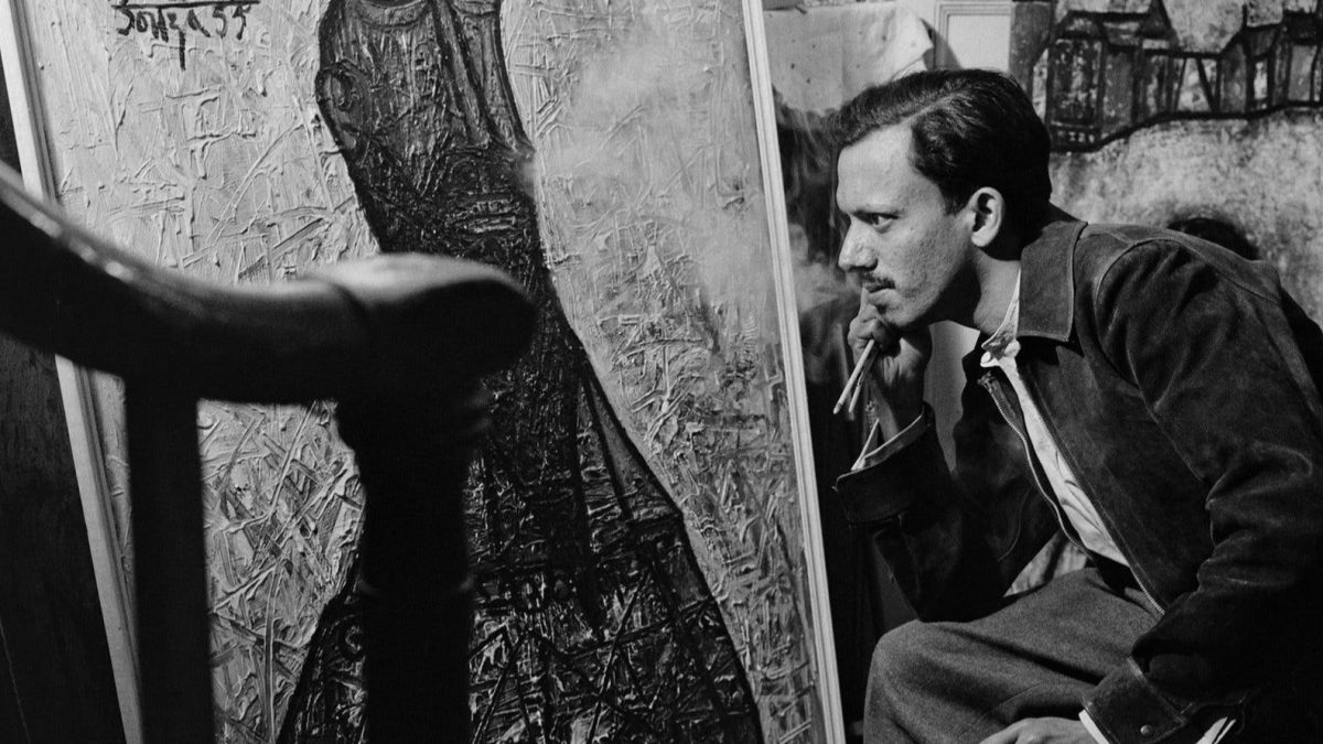 A black-and-white photograph of F. N. Souza seated before one of his paintings
