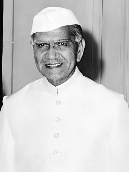 A black-and-white portrait of Fakhruddin Ali Ahmed in a white cap and white achkan, smiling