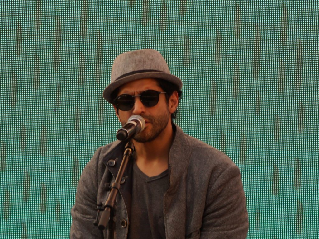 Farhan Akhtar in a hat and sunglasses singing into a microphone on stage
