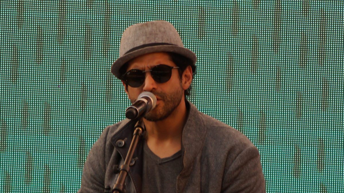 Farhan Akhtar in a hat and sunglasses singing into a microphone on stage