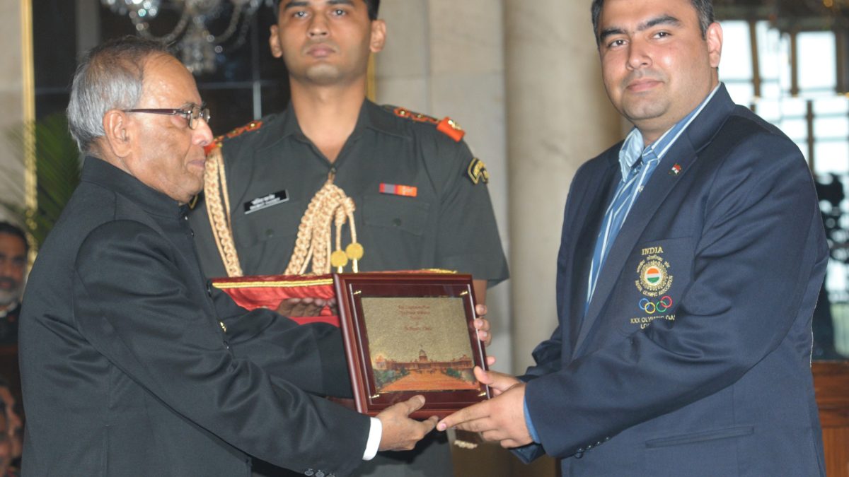 Gagan Narang in a navy blazer receiving a memento from President Pranab Mukherjee