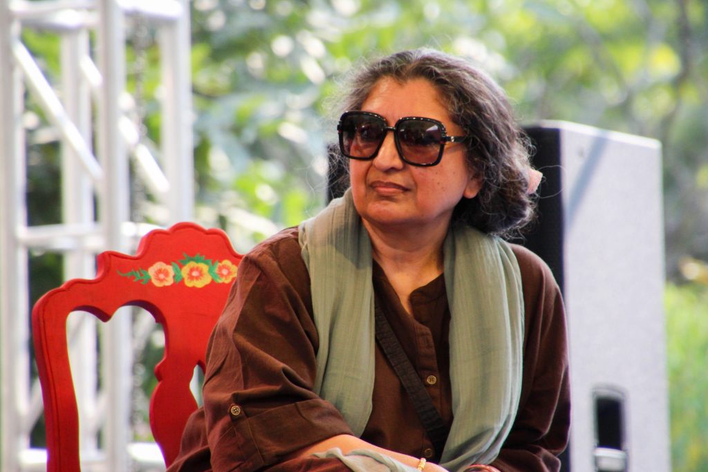 Geetanjali Shree with grey hair in sunglasses and a green scarf, seated outdoors