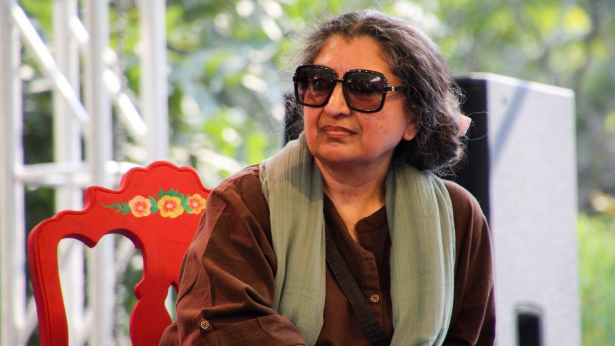 Geetanjali Shree with grey hair in sunglasses and a green scarf, seated outdoors