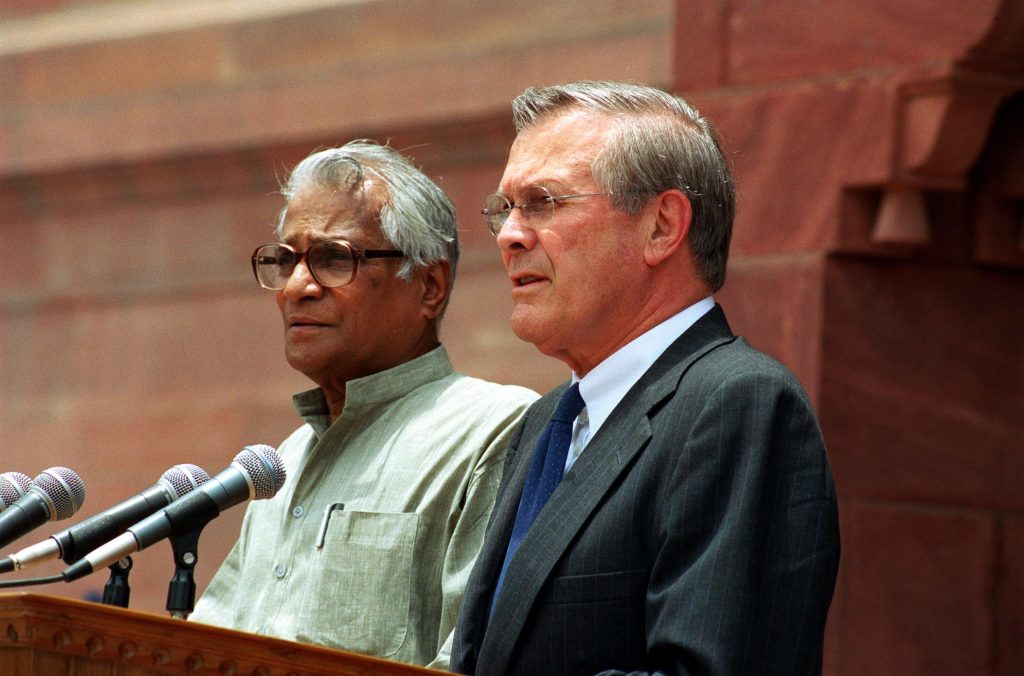 George Fernandes in a white kurta speaking at a lectern beside Donald Rumsfeld