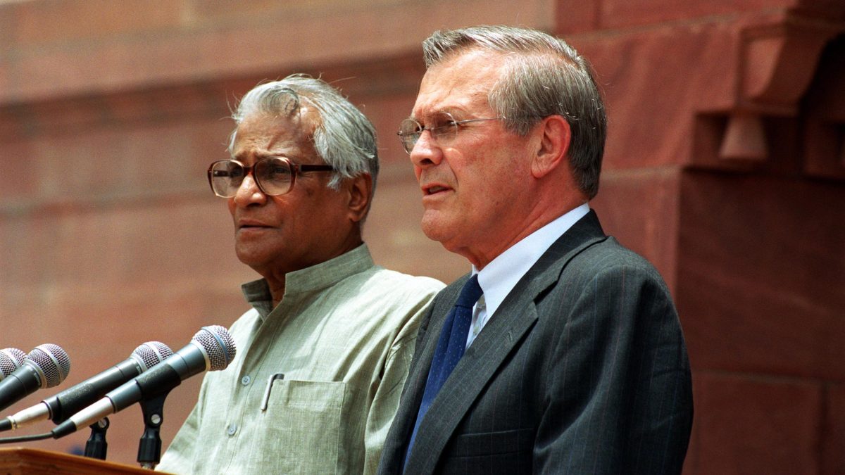 George Fernandes in a white kurta speaking at a lectern beside Donald Rumsfeld