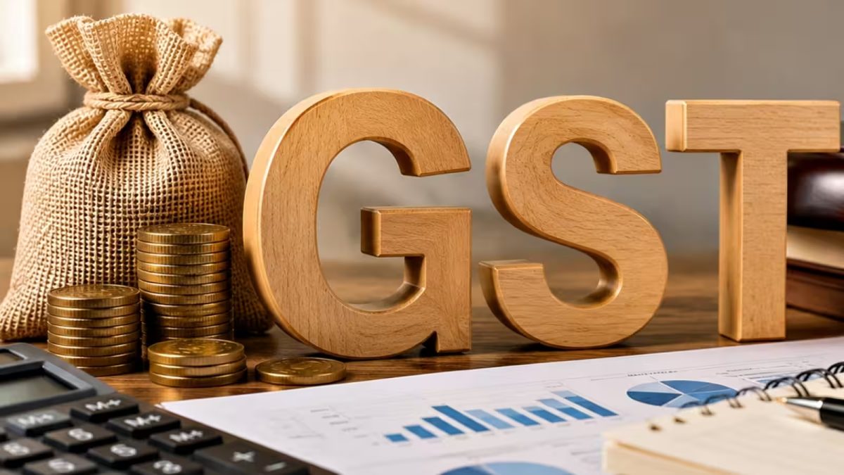 Wooden letters spelling GST with coins, a calculator and charts on a desk