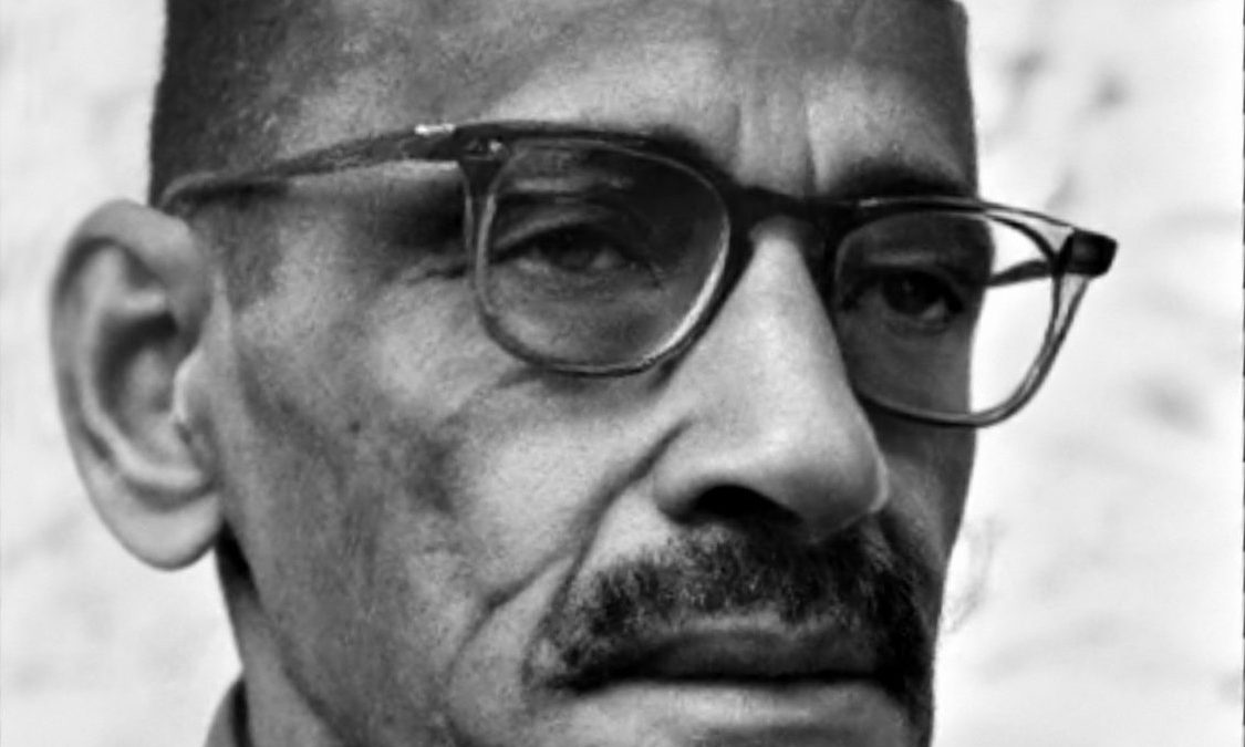 A black-and-white photograph of Gulzarilal Nanda in a Gandhi cap and glasses