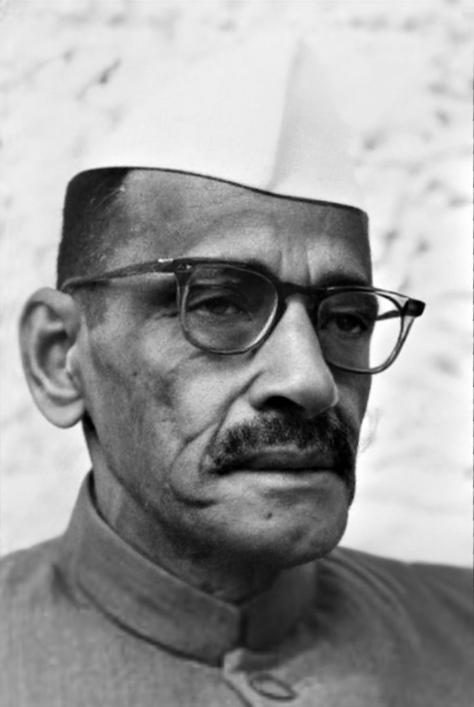 A black-and-white photograph of Gulzarilal Nanda in a Gandhi cap and glasses