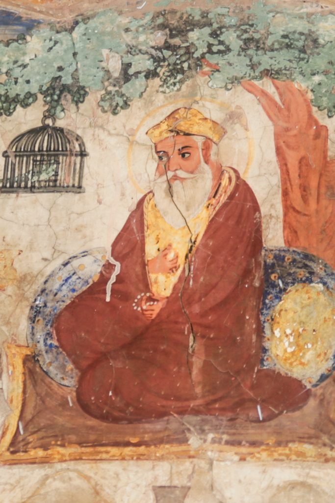 A mural painting of Guru Nanak seated with a halo, attended by companions