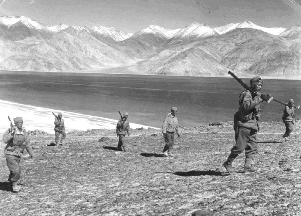 A black-and-white photograph of Indian soldiers on patrol beside a lake in the mountains during the 1962 border war