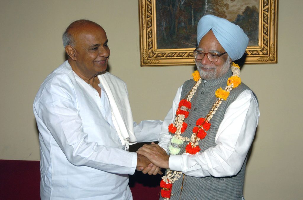 H. D. Deve Gowda in white garlanding and shaking hands with Prime Minister Manmohan Singh