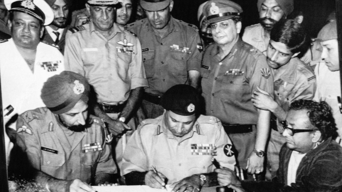 Lt Gen A. A. K. Niazi signing the Instrument of Surrender beside Lt Gen Jagjit Singh Aurora at Dhaka on 16 December 1971, with Indian officers standing behind