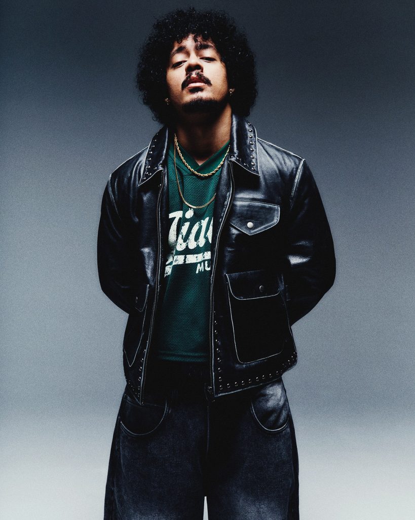Hanumankind with curly hair in a black leather jacket, head tilted back