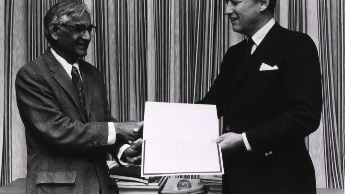 Har Gobind Khorana in a dark suit and glasses receiving a certificate from another man