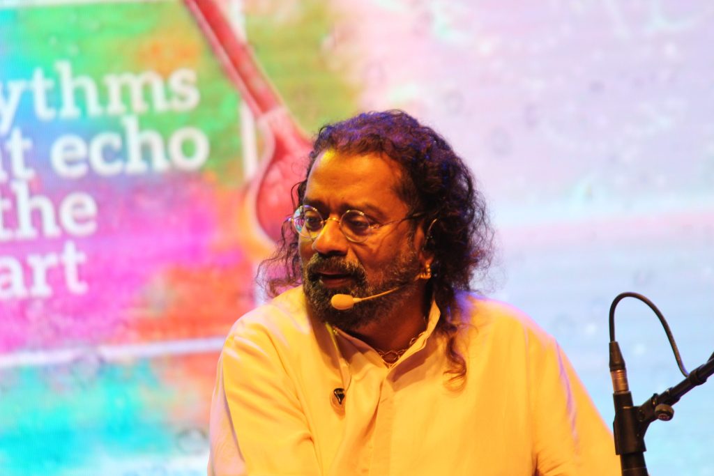 Hariharan with long curly hair and a headset microphone, wearing a yellow kurta