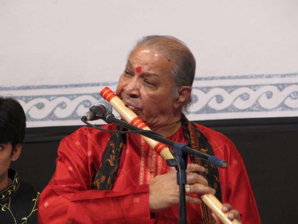 Hariprasad Chaurasia in a red kurta playing the bamboo flute on stage