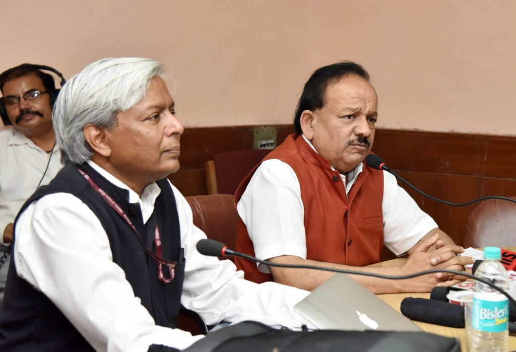 Harsh Vardhan in glasses and a saffron waistcoat speaking at a press conference beside an official