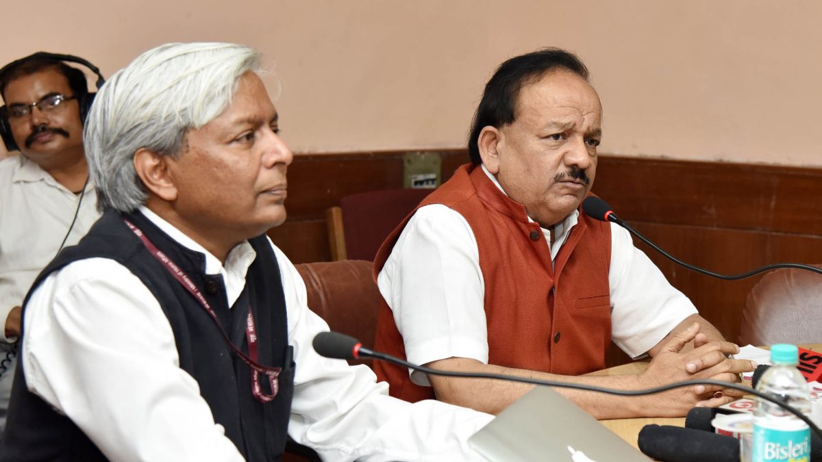 Harsh Vardhan in glasses and a saffron waistcoat speaking at a press conference beside an official