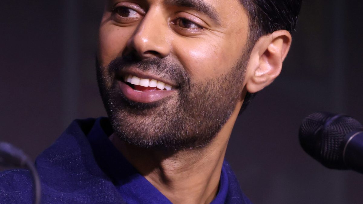 Hasan Minhaj smiling as he speaks into a microphone