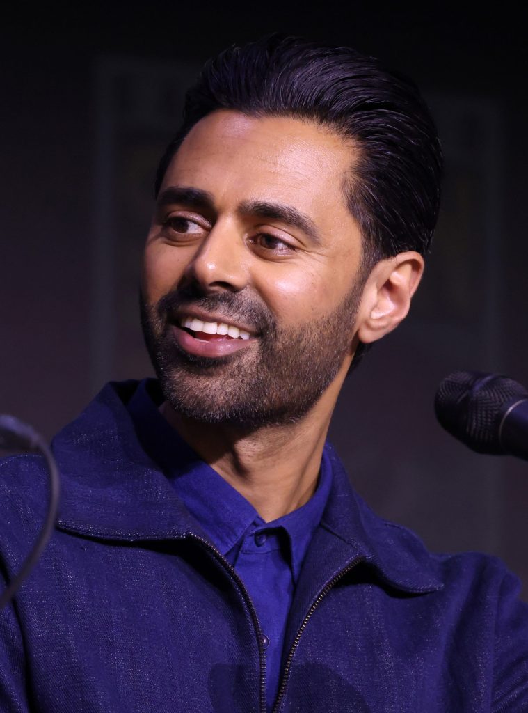 Hasan Minhaj smiling as he speaks into a microphone
