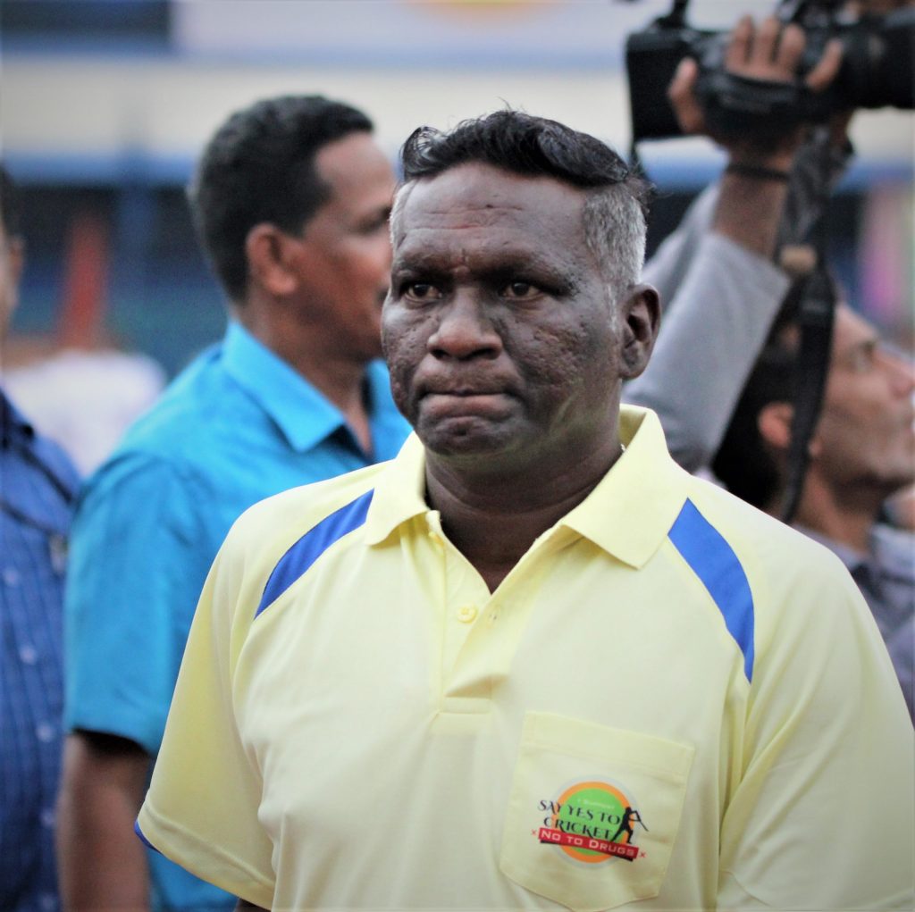 I. M. Vijayan in a yellow polo shirt at a stadium, with cameramen behind him