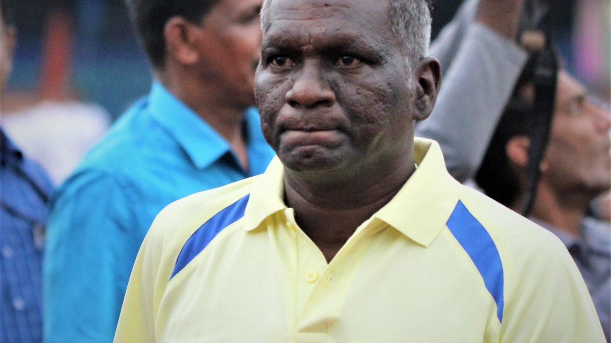 I. M. Vijayan in a yellow polo shirt at a stadium, with cameramen behind him