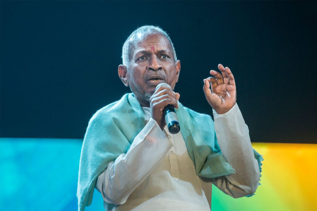 Ilaiyaraaja in a white kurta and green shawl speaking into a microphone
