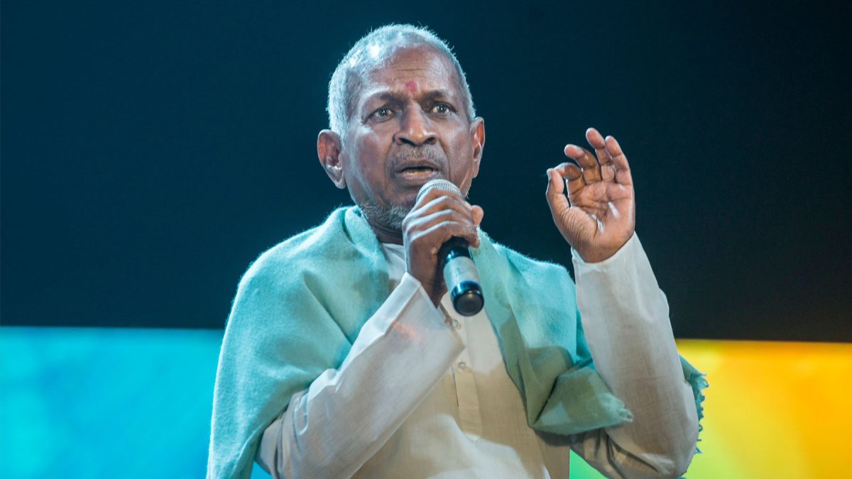 Ilaiyaraaja in a white kurta and green shawl speaking into a microphone